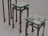 trois tables avec un plateau en verre et des pieds en métal, sur fond gris