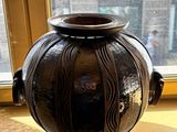 un vase noir posé sur une table devant une fenêtre