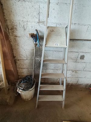 une échelle appuyée contre un mur, à côté d'un seau rempli d'outils