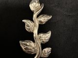 a close up of a silver brooch with leaves on a black background