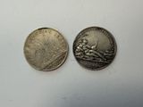 two silver coins sitting next to each other on a white surface