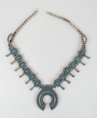 un collier composé de pierres turquoise et de perles en argent sur fond blanc