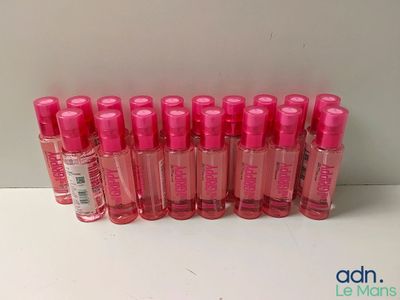 Neuf flacons de parfum rose sont alignés sur une surface blanche
