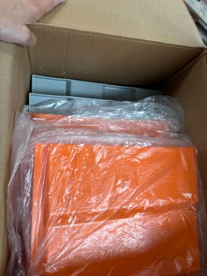 a person holding a box full of orange shirts