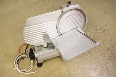 a meat slicer sitting on the floor next to a cord