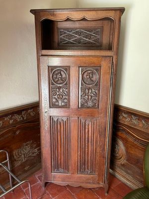 a tall wooden cabinet in the corner of a room with a green chair