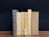 several old books are stacked on a wooden shelf against a black wall
