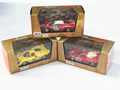 trois petites voitures rouges et jaunes dans leurs boîtes, posées sur une surface blanche