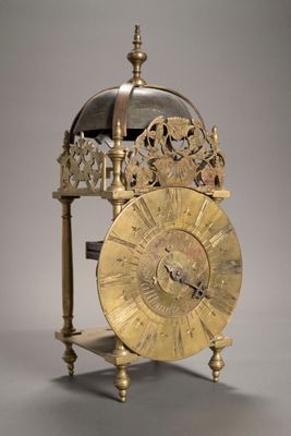 une horloge dorée posée sur un socle, sur fond gris