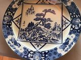 a blue and white plate on a table with a person standing next to it