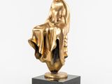 une statue en or représentant une femme assise sur un bloc de marbre