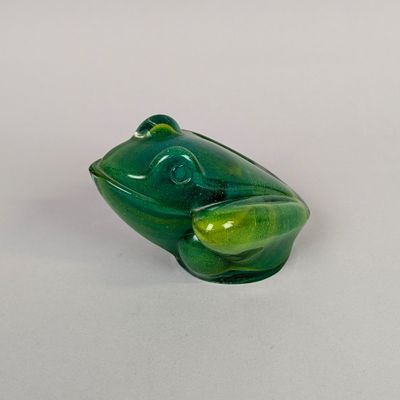 une figurine de grenouille en verre posée sur une surface blanche