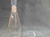 une bouteille en verre avec un bouchon argenté, posée à côté d'un cendrier en verre