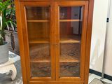 a wooden cabinet with glass doors and a plant in the corner