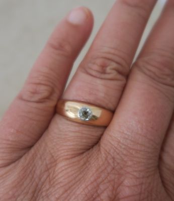 a person ' s hand holding a gold ring with a diamond on it