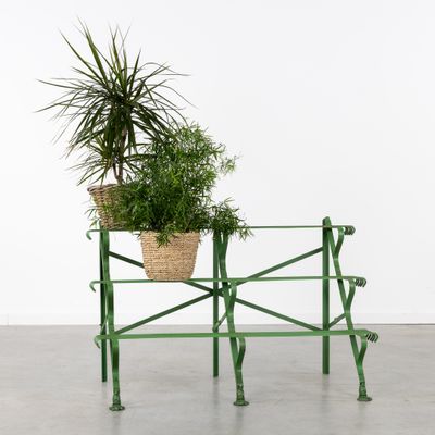 a green metal bench with a plant in a basket on top of it