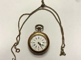 une montre de poche en or avec une chaîne, posée sur une surface blanche
