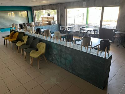 Des chaises aux couleurs vives sont disposées autour d'une longue table dans une grande pièce.