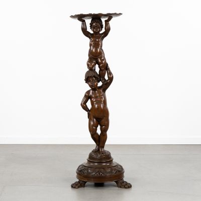une statue en bronze représentant un garçon tenant un bol, posée sur un socle