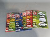 four magazines of different cars on a table with a white car in the background