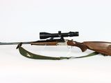 the rifle is laying on the ground with a scope on it ' s side