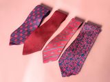 three ties are lined up on a pink surface, one is red and the other is blue