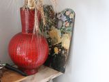 a red vase sitting on top of a wooden shelf next to a pair of scissors
