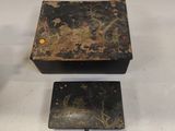 two black boxes with gold designs on them sitting on a white surface