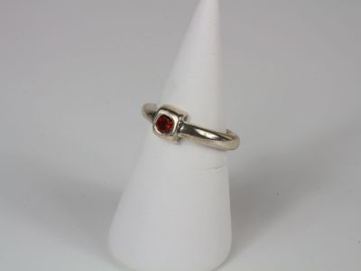 a close up of a ring on a white cone with a red stone