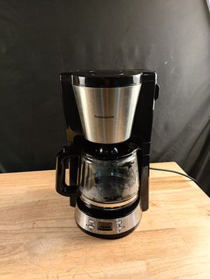 une cafetière posée sur une table en bois, avec un mur noir en arrière-plan