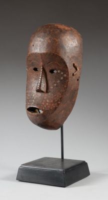un masque en bois posé sur un socle, sur fond gris