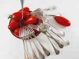 tomatoes in a bowl with forks and spoons on a white surface