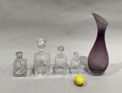 a purple glass vase, a bottle, and a banana on a white surface