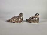 deux oiseaux argentés, perchés l'un sur l'autre, sur une surface blanche