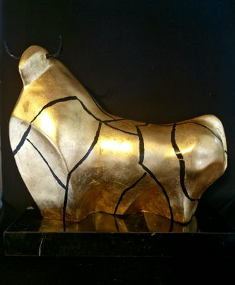 une statue représentant un taureau doré posée sur une table noire