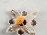 a silver and yellow flower brooch on a white surface