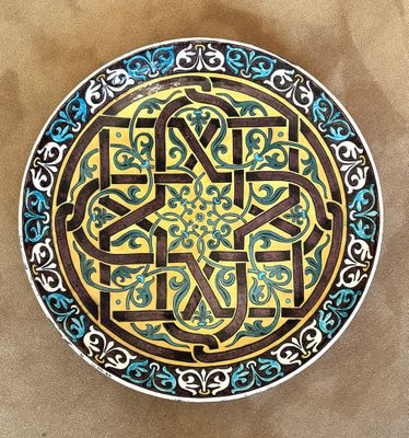 peinture représentant une assiette décorative ornée de motifs bleus et jaunes sur fond marron