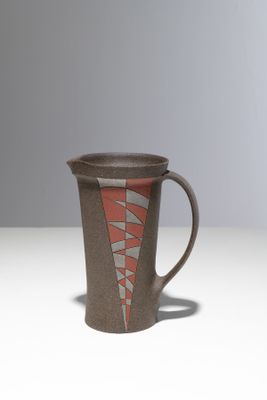 une tasse marron et rouge posée sur une table blanche, sur fond gris