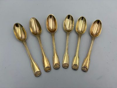 six cuillères en or sont alignées sur une table