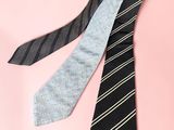 two ties are laying on a pink surface, one is black and the other is light blue