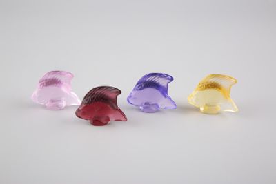quatre figurines d'animaux en plastique de couleurs différentes posées sur une surface blanche