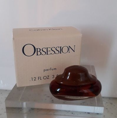 un flacon de parfum posé sur une boîte transparente, à côté d'une boîte en carton