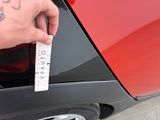 a person holding a measuring tape near a red car