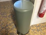 a green trash can sitting on the floor in a bathroom