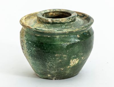 un vase vert muni d'un couvercle, posé sur une surface blanche