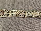 silver metal bracelet with intricate design on it on a gray cloth