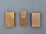 three gold lighters sitting side by side on a blue surface
