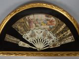 a gold frame holding a fan and a painting on the wall
