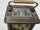 a small metal clock with a brass handle on a white surface