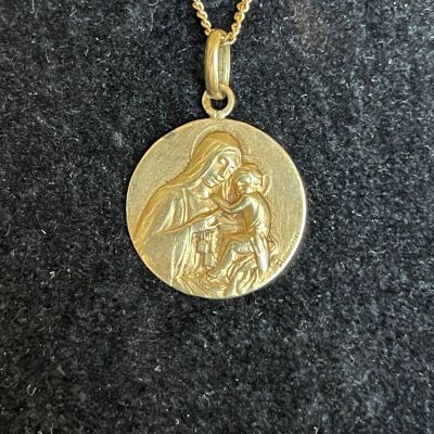 a close up of a gold plated necklace with a picture of a woman holding a child